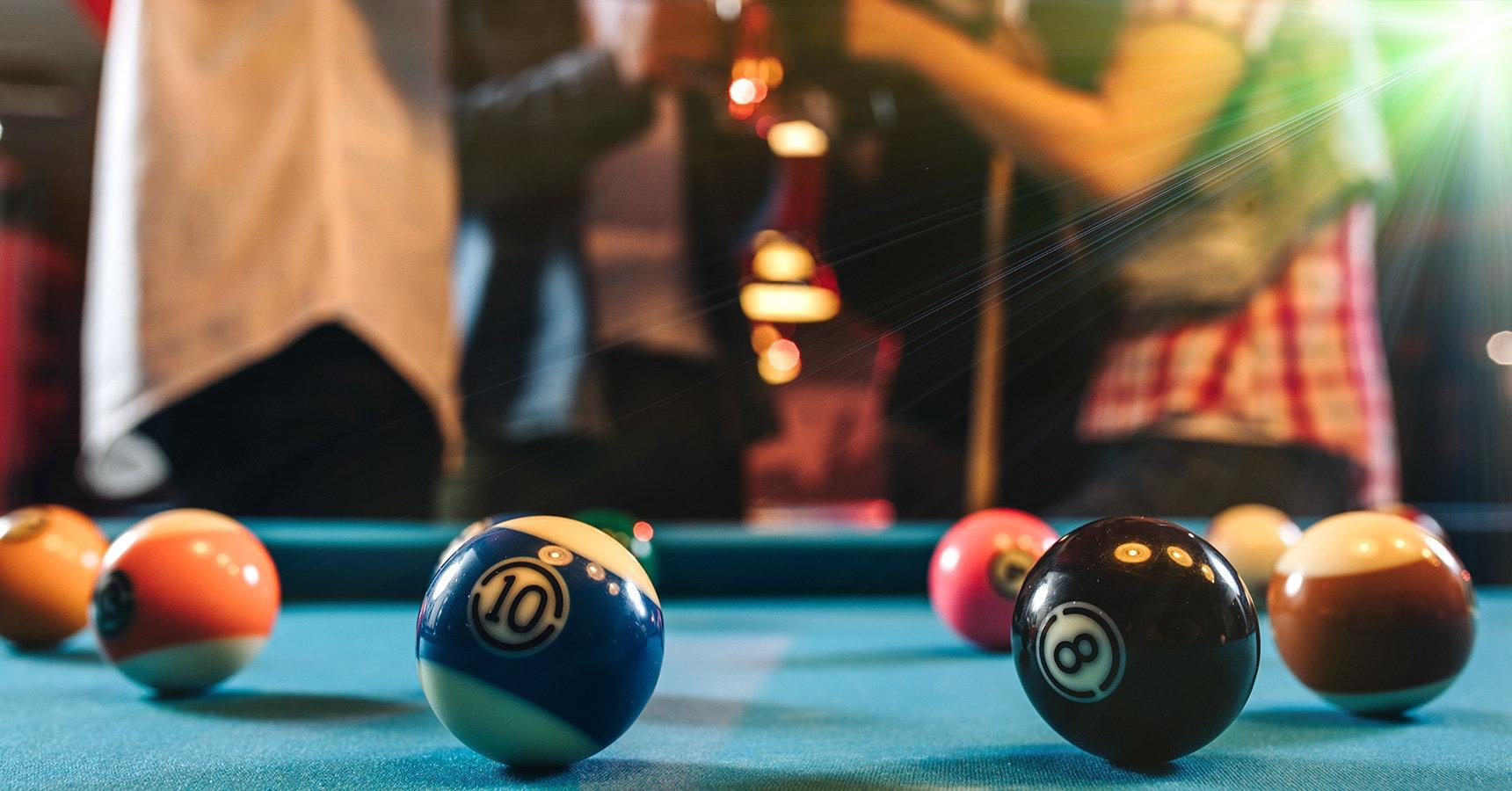 Billiards table with balls in the foregound and people socializing in the background