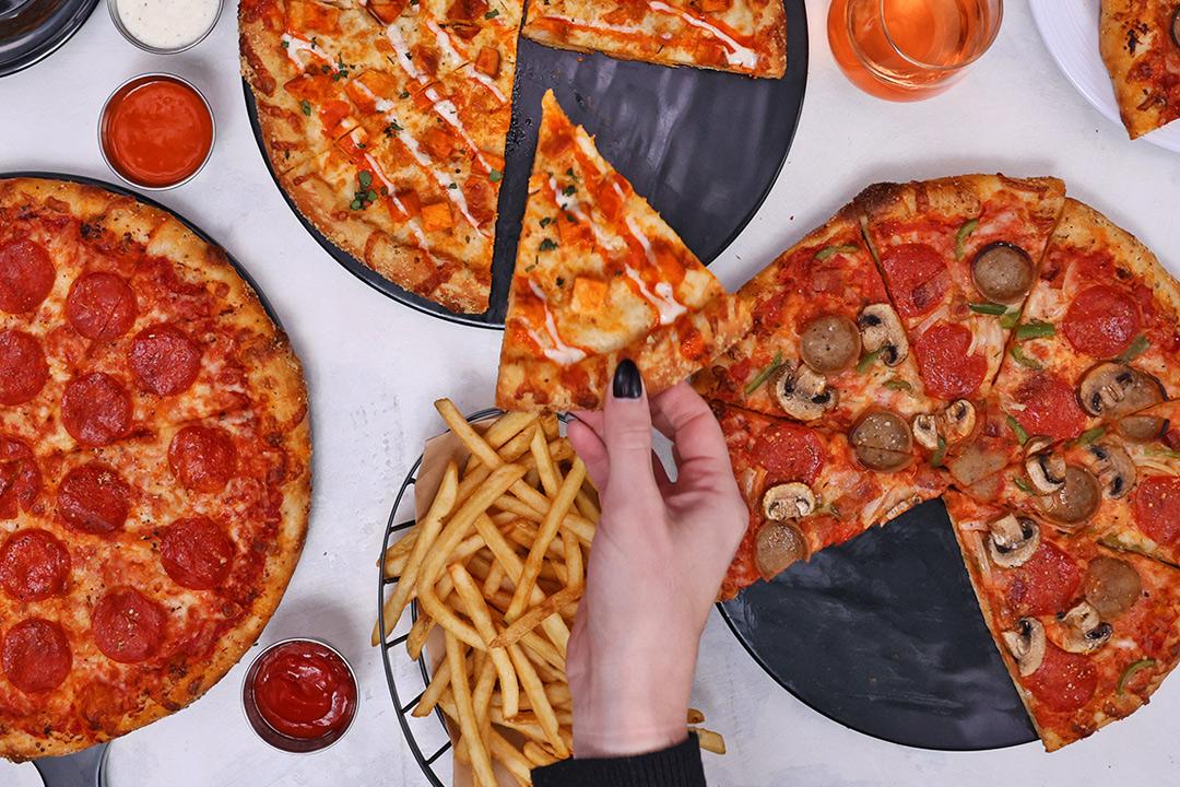 A hand grabbing a slice of pizza with french fries. 