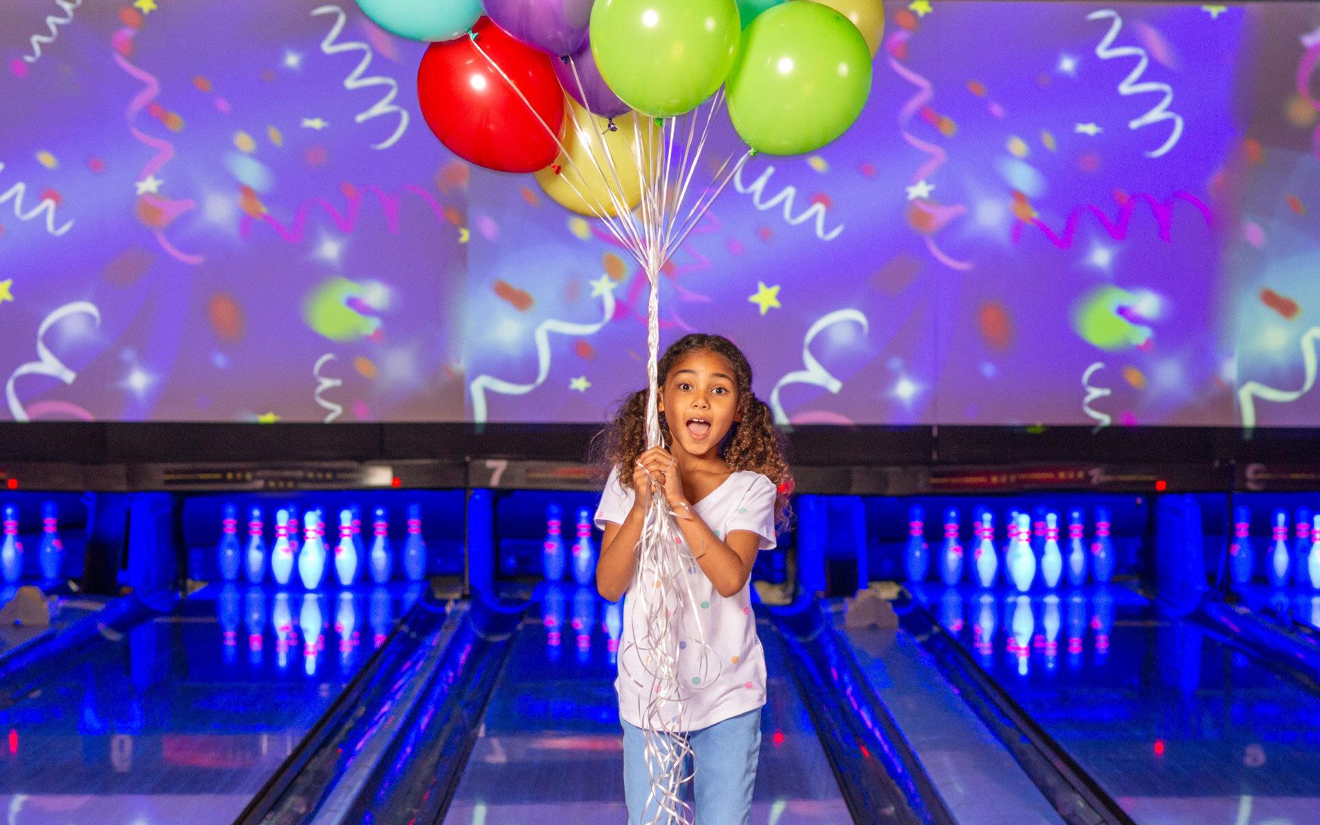 A girl holding up a balloon on bowling lanes.