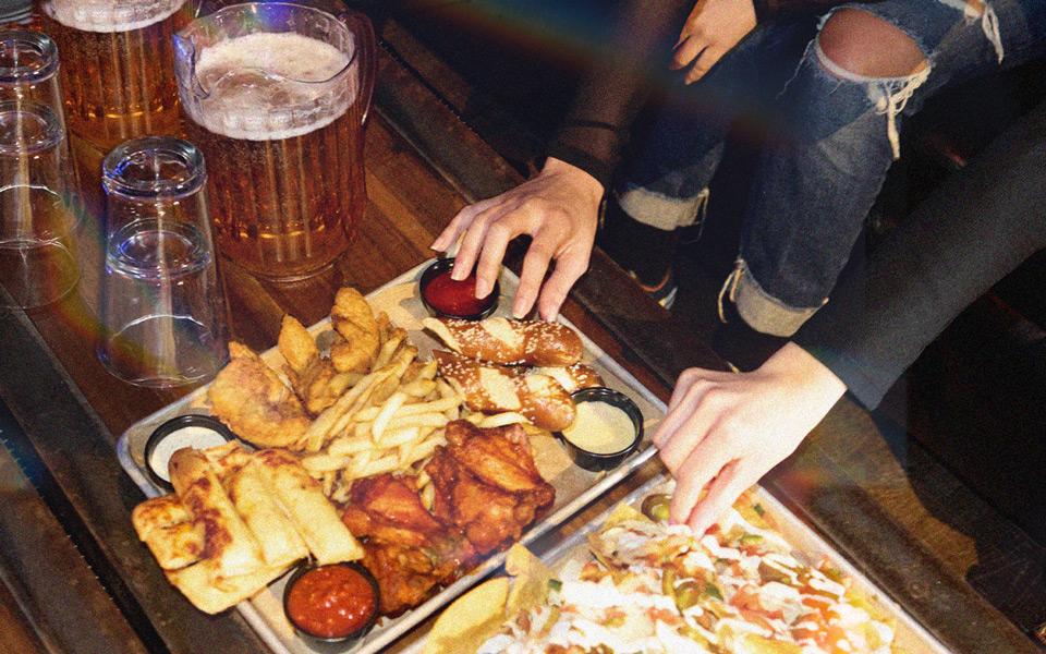 Two friends grab delicious food while bowling with pitchers of beer and cocktails. 