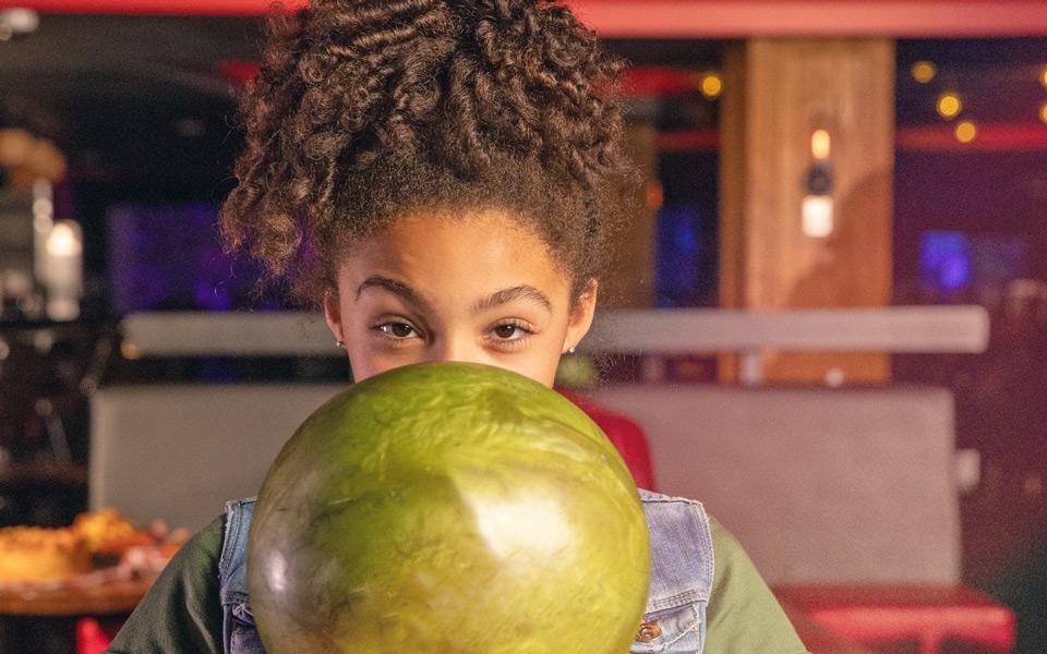 A girl holding a bowling ball looking at the camera. 