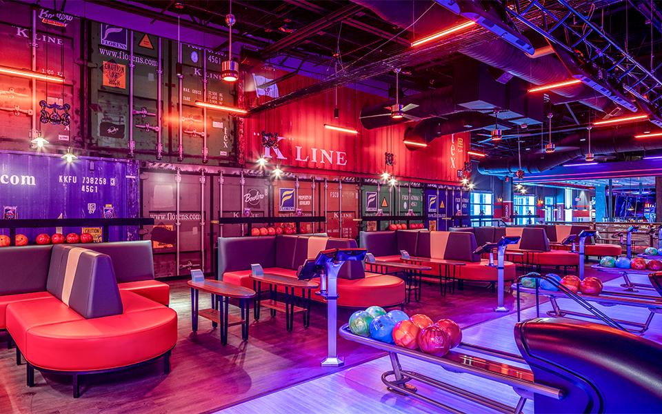 Colorfully lit bowling center showing tables and ball returns