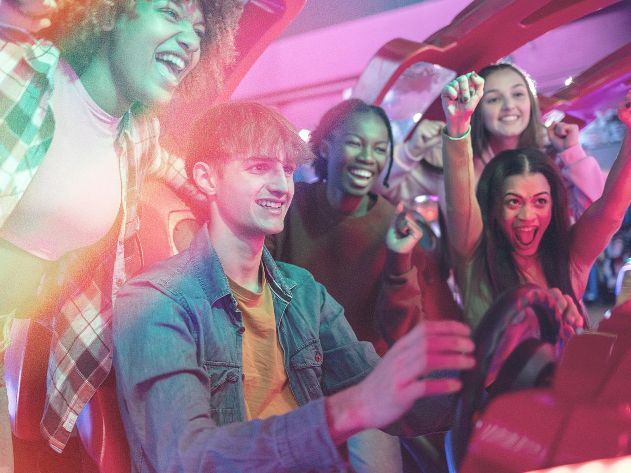 A group of teenagers playing an arcade game. 