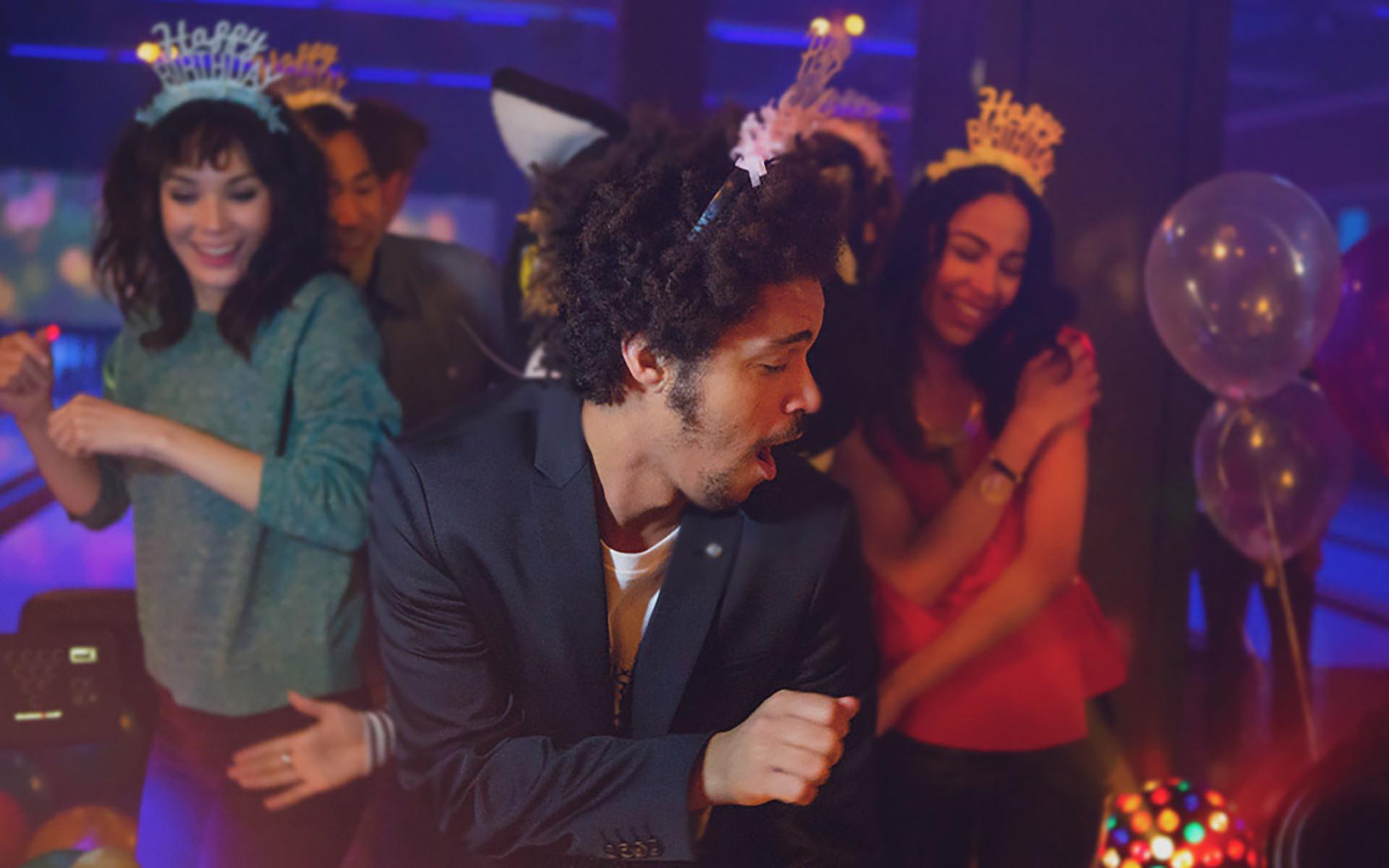 Adult man dancing and having fun on the lanes with a group of friends wearing happy birthday hats. 